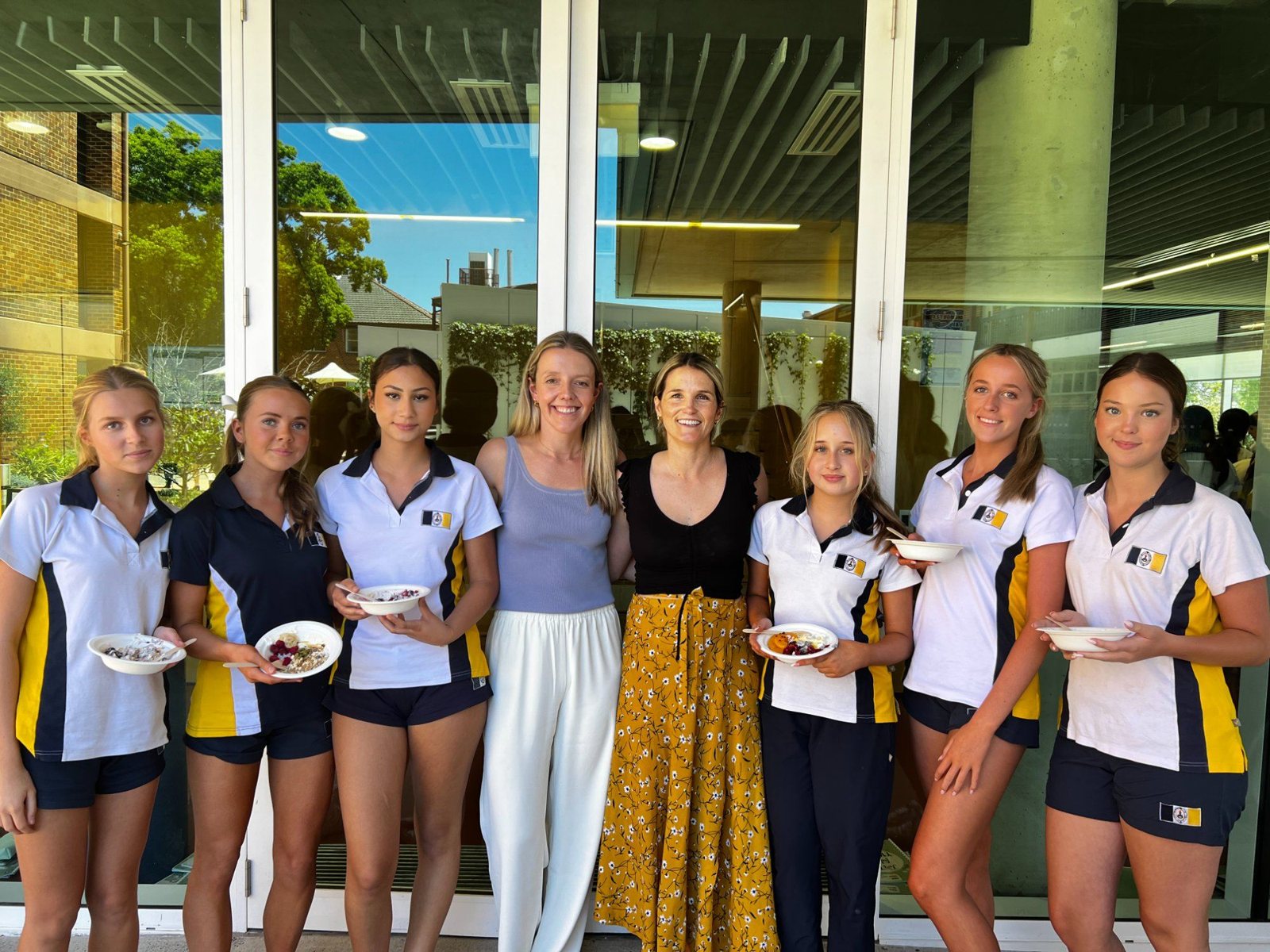 Two dietitians from The Biting Truth with six students holding bowls from a hands-on nutrition workshop
