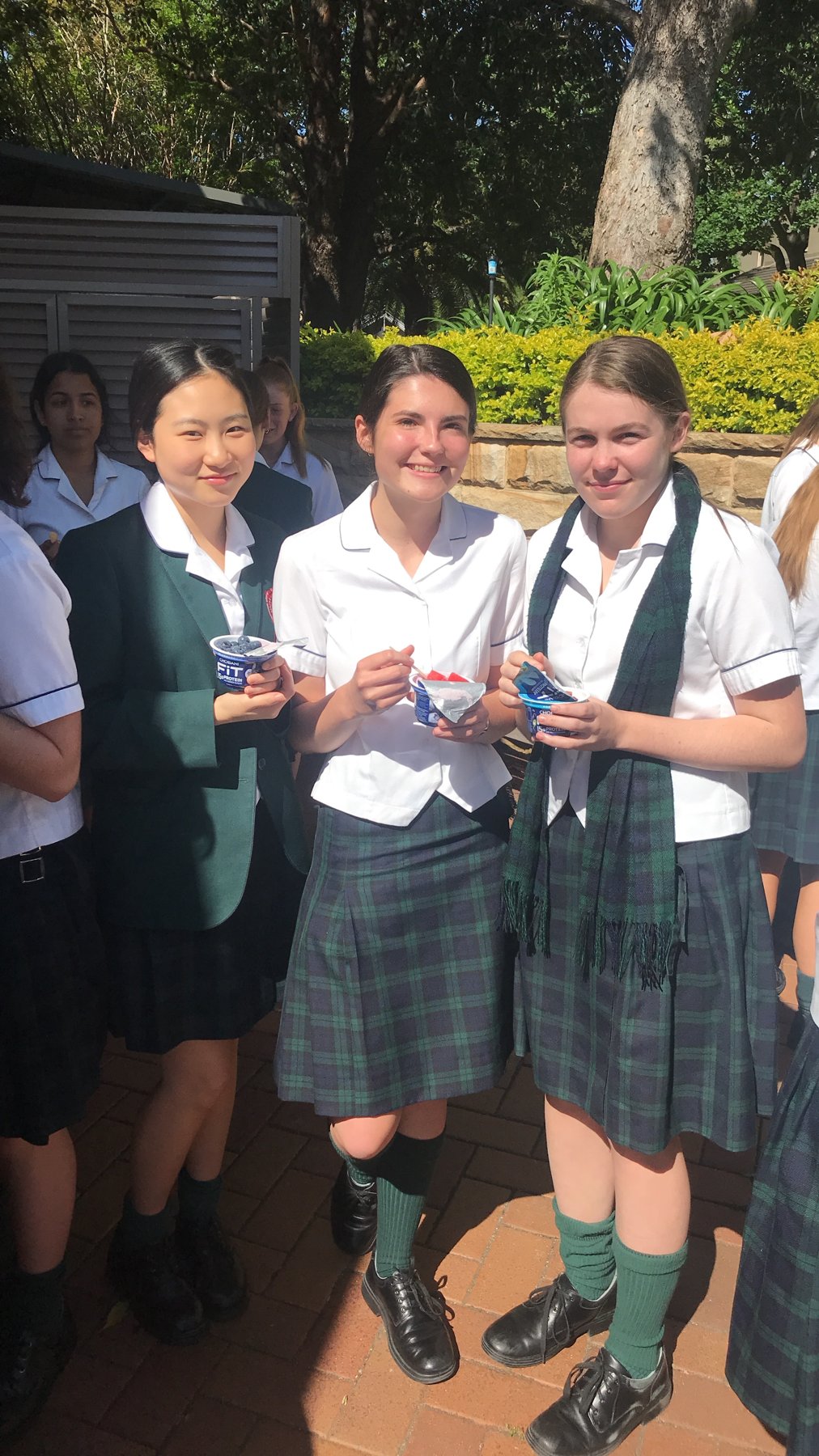 Three students in school uniform smiling and eating yoghurt and fruit after a Fuel Your Potential nutrition session